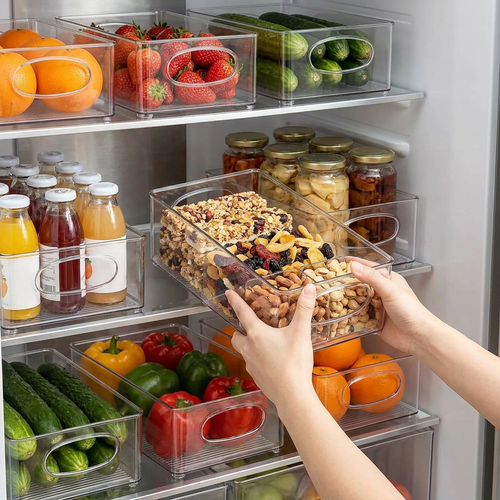 Person sliding a clear organiser bin full of snacks onto a fridge shelf