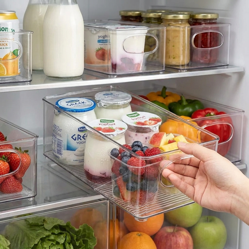 Hand pulling a clear fridge bin out by its handle, filled with yoghurts and fruit